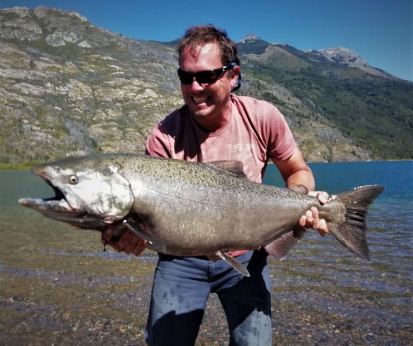 Pescador sosteniendo un gran salmón Chinook frente a Lago Puelo